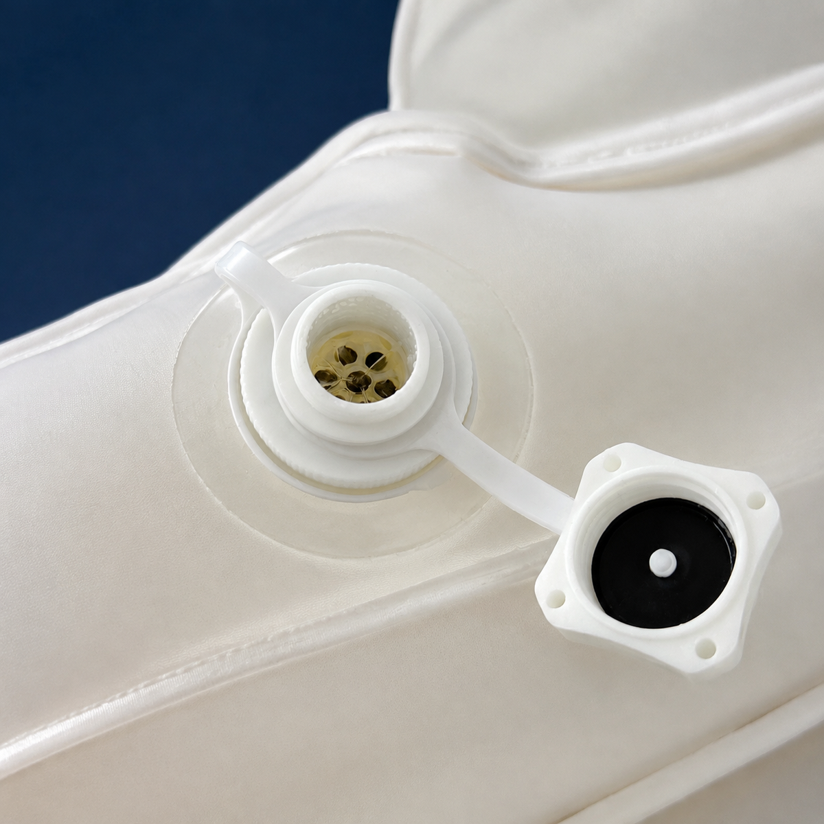 Close-up of a white inflatable or flexible plastic bag with two circular openings, one showing a small gold-colored filter or mesh and the other with a black insert, set against a dark blue background.