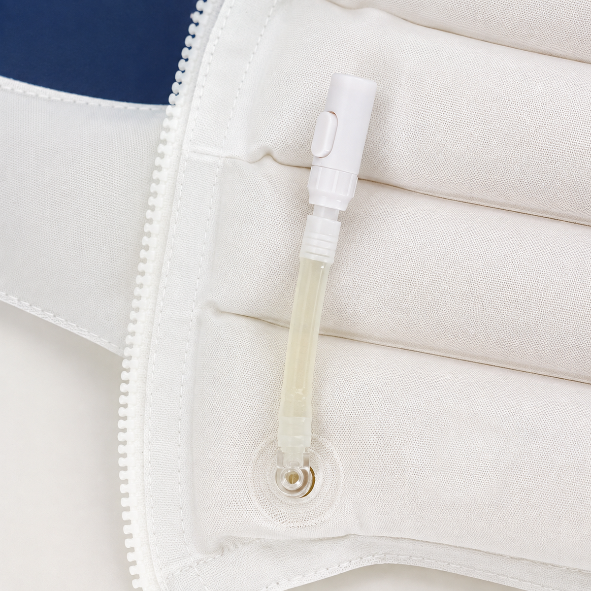 Close-up of a white padded support or compression sleeve with a clear plastic tube and white cap attached near a zipper.